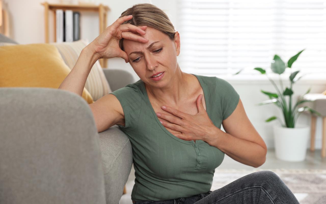 Mulher sentada sentindo mal estar por causa dos sintomas do climatério.